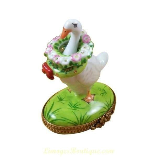 Porcelain Limoges box shaped like a white goose with a floral wreath standing on a green base for collecting Limoges porcelain boxes