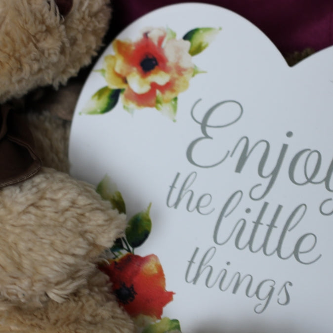 a teddy bear holding a sign that says enjoy the little things