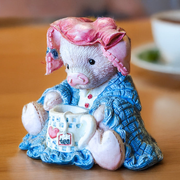 A ceramic pig figurine holding a teacup.