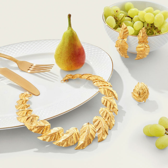 Gold leaf jewelry, pear, grapes, and cutlery on white.